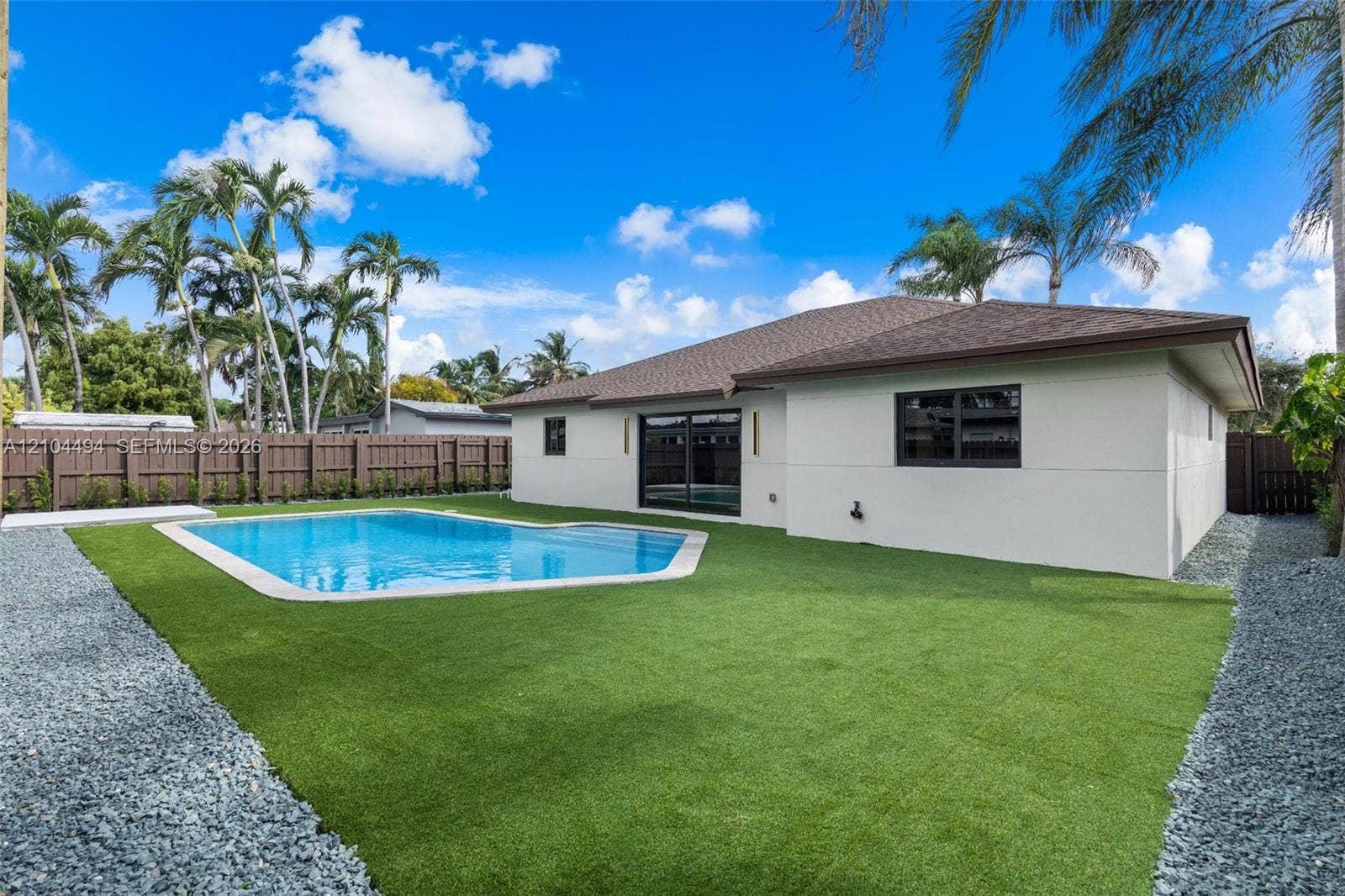 711 NW 8th Avenue, Dania Beach, FL 33004 Backyard featuring an in-ground swimming pool, synthetic turf lawn, stone-surfaced side border, and wood-finish privacy fencing