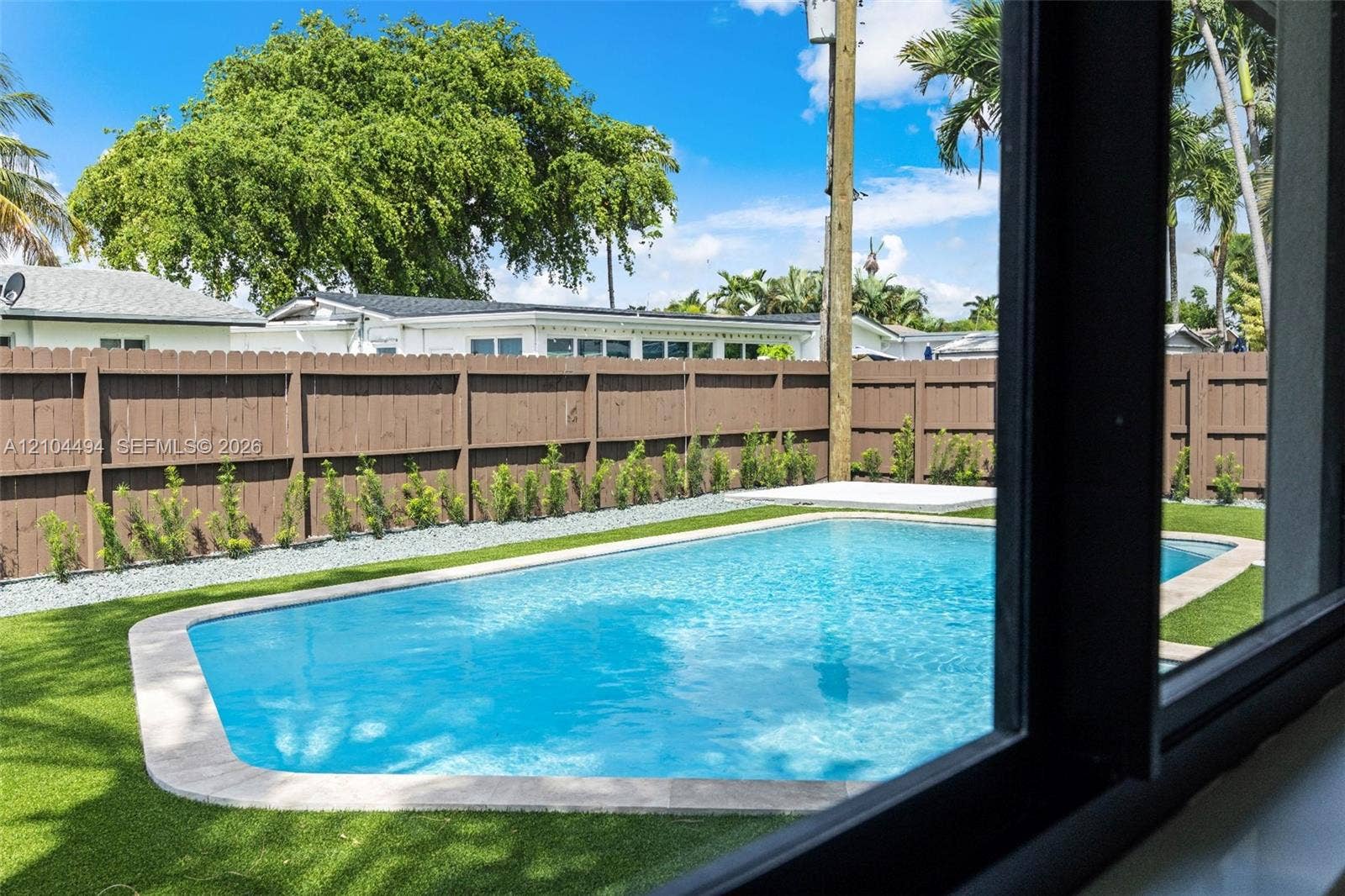 711 NW 8th Avenue, Dania Beach, FL 33004 Outdoor space featuring a swimming pool with stone coping, synthetic turf lawn, wood privacy fencing, and perimeter landscaping