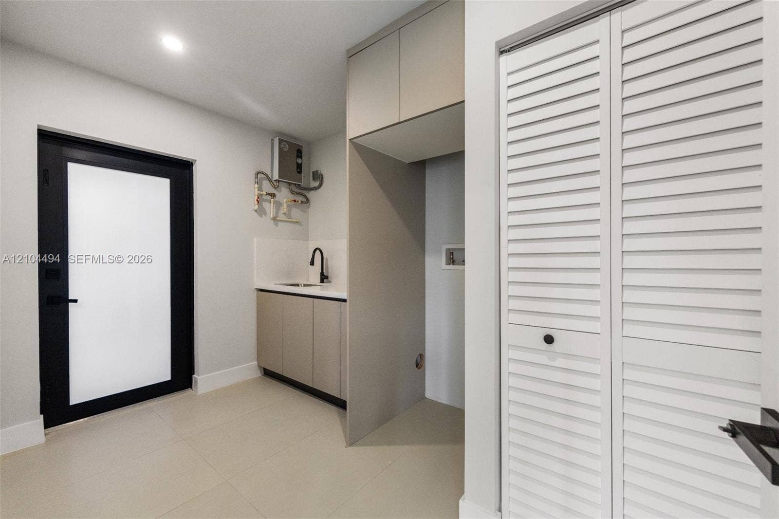 711 NW 8th Avenue, Dania Beach, FL 33004 Utility space featuring custom cabinetry, integrated sink with matte black fixture, louvered closet doors, and black-framed glass-panel door