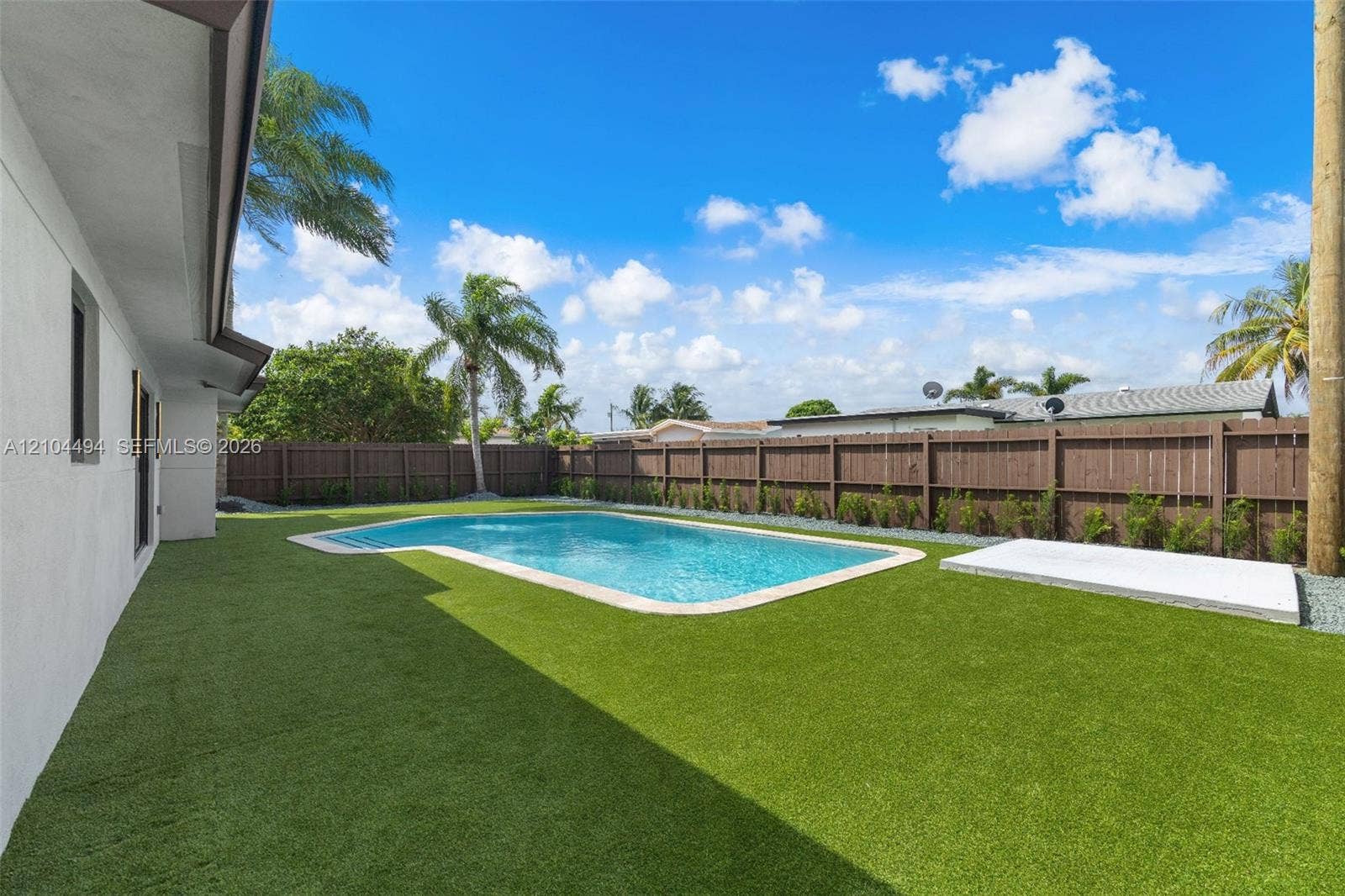 711 NW 8th Avenue, Dania Beach, FL 33004 Outdoor living area featuring an in-ground swimming pool, artificial turf, perimeter wood fencing, and a concrete patio slab