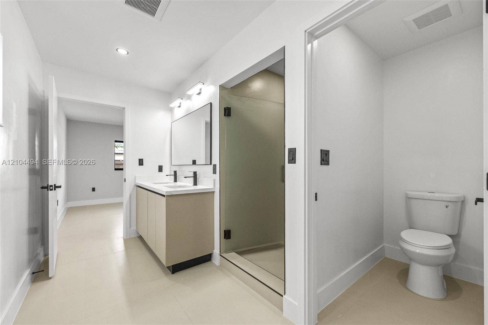 711 NW 8th Avenue, Dania Beach, FL 33004 Bathroom featuring a floating vanity with a light-tone finish, rectangular dual-basin countertop, glass-enclosed shower with matte black hardware, and tile flooring