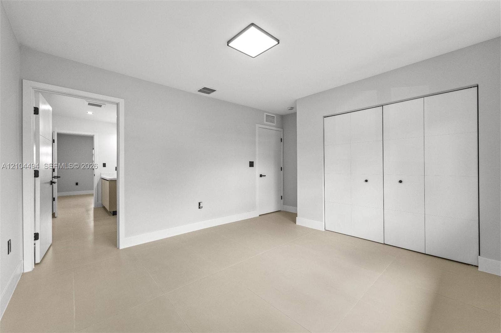 711 NW 8th Avenue, Dania Beach, FL 33004 Neutral-toned interior space featuring light-colored tile flooring, flush-mount square ceiling lighting, and a multi-panel sliding closet system with matte black hardware
