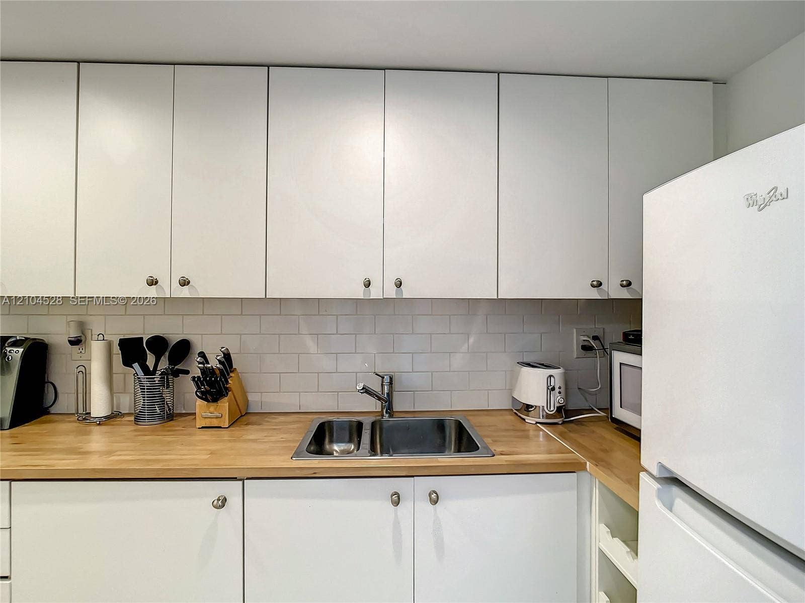 Kitchen featuring white flat-panel cabinetry, light wood-finish countertops, stainless steel dual-basin undermount sink, and white subway tile backsplash