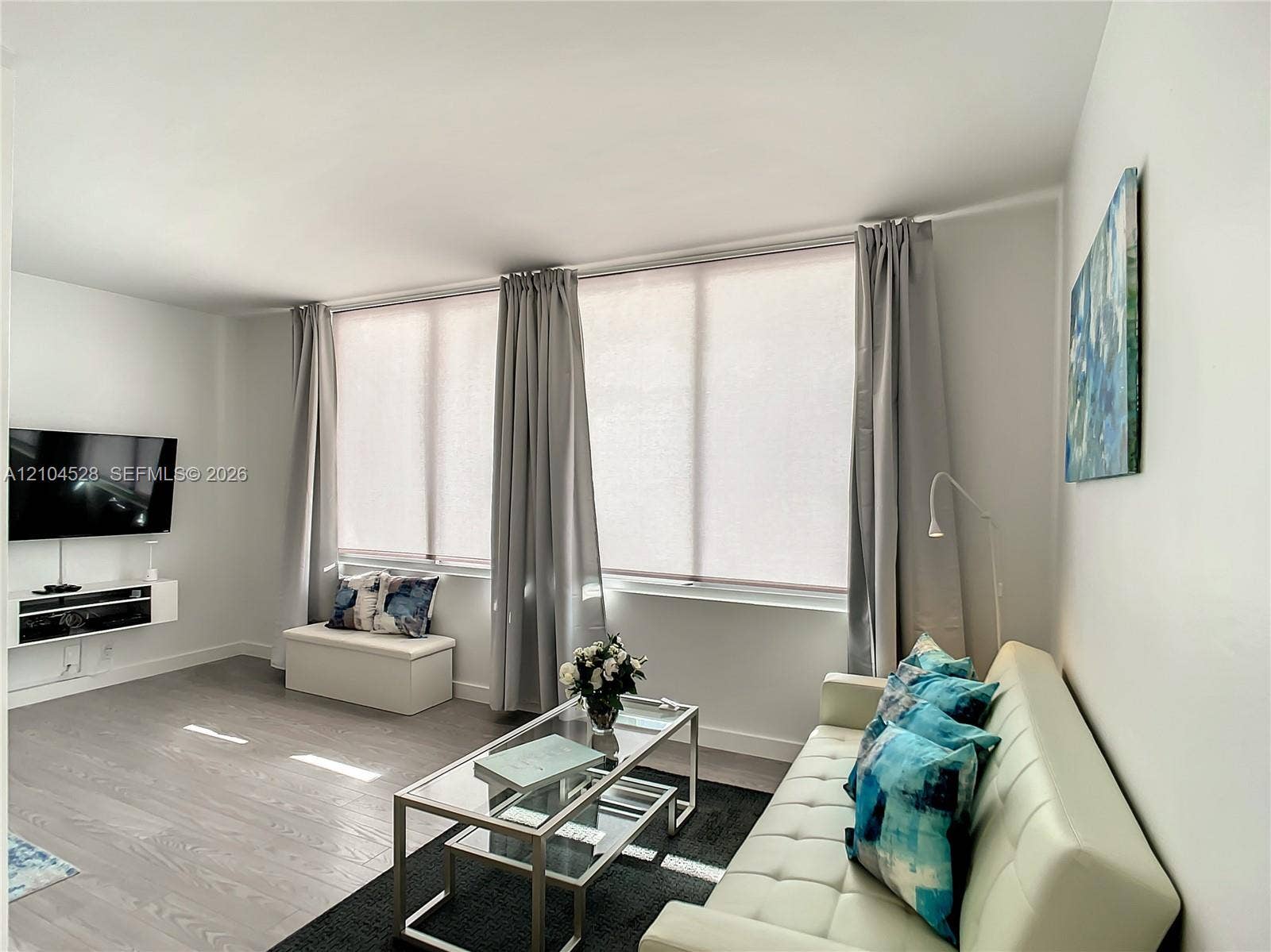 Living area featuring large windows with natural light, wood-finish flooring, and a white wall-mounted media console