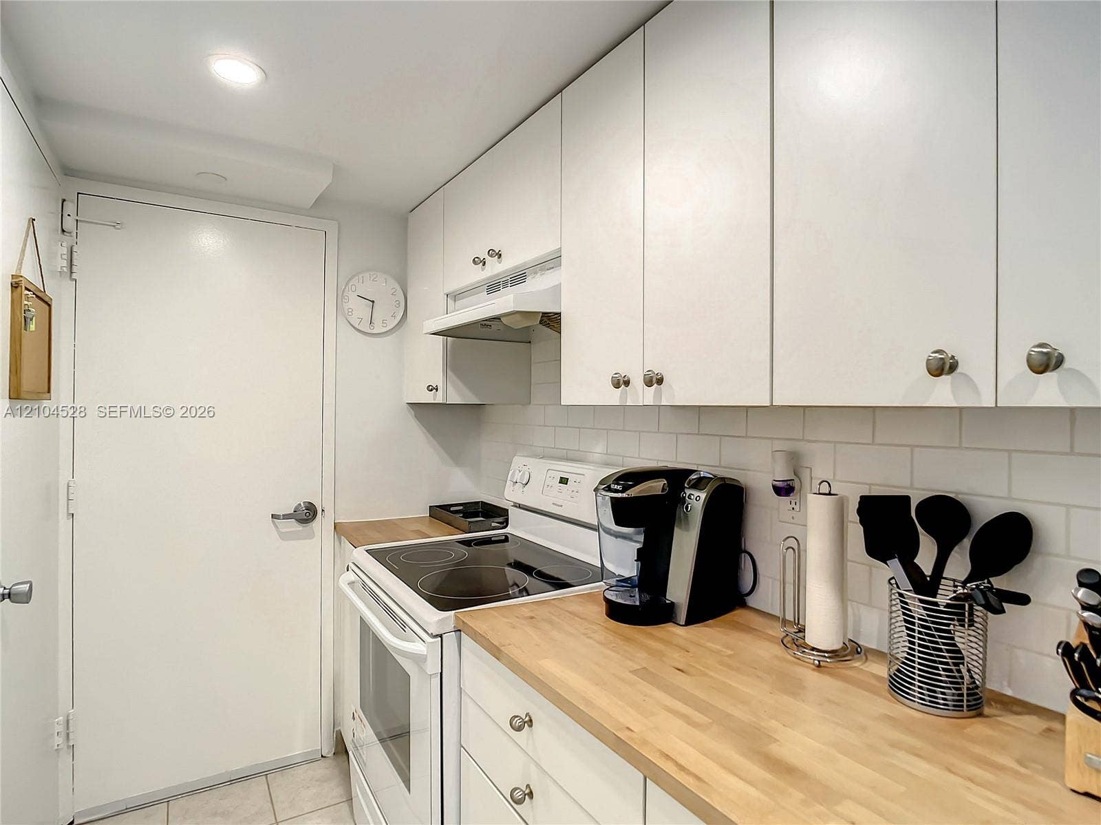 Kitchen featuring white cabinetry, wood-finish countertops, subway tile backsplash, and an integrated range hood