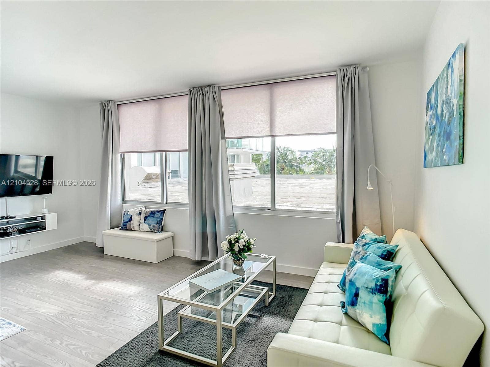 Neutral wall-to-wall wood-finish flooring, expansive windows with integrated roller shades, and a wall-mounted floating media console