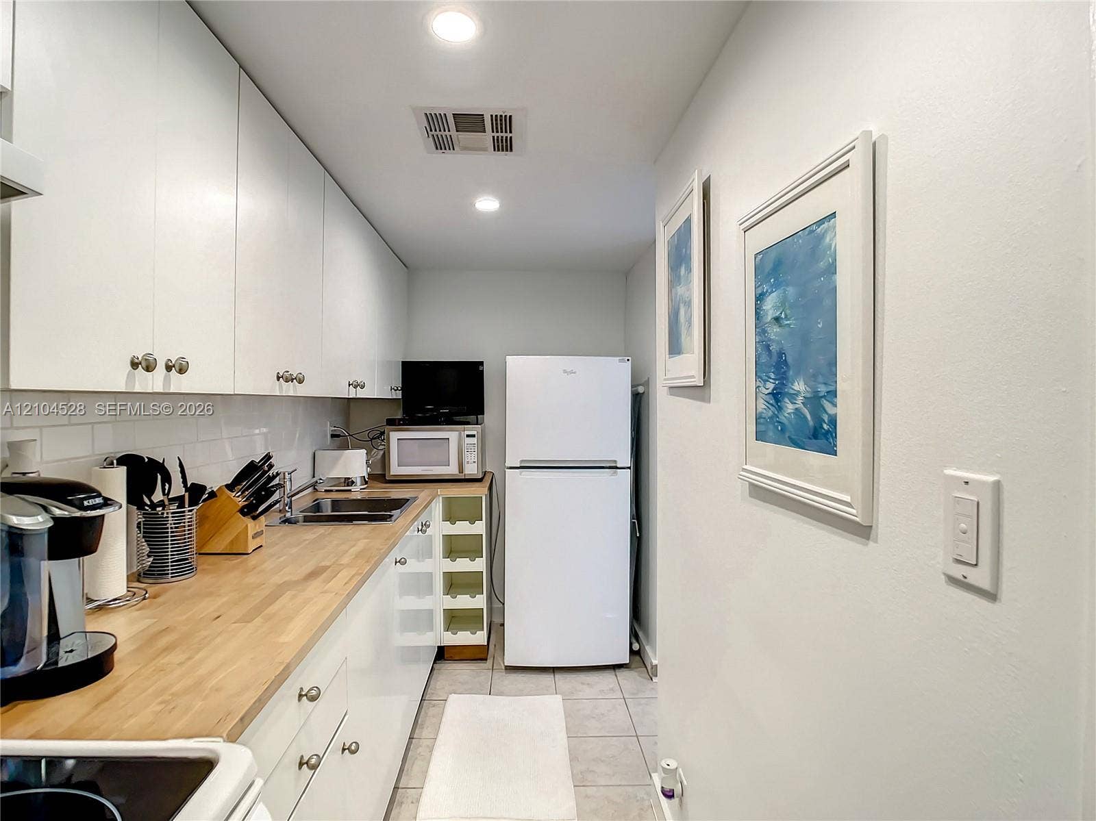 Kitchen featuring white flat-panel cabinetry, light-toned wood-finish countertops, white subway tile backsplash, recessed lighting, and tile flooring