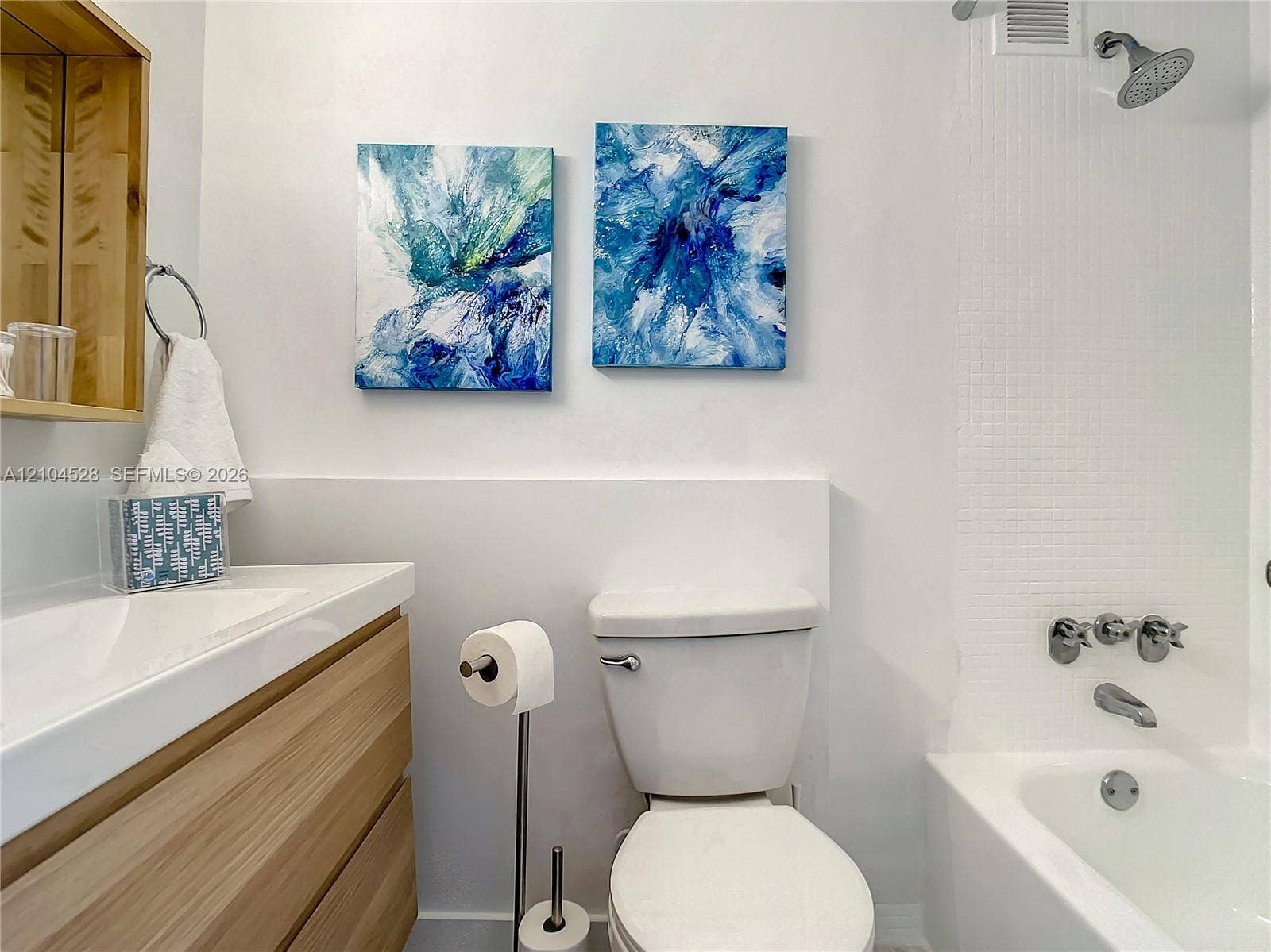 Bathroom featuring a wood-finish floating vanity, integrated rectangular sink, wall-mounted medicine cabinet, and a tiled shower-tub combination with chrome fixtures