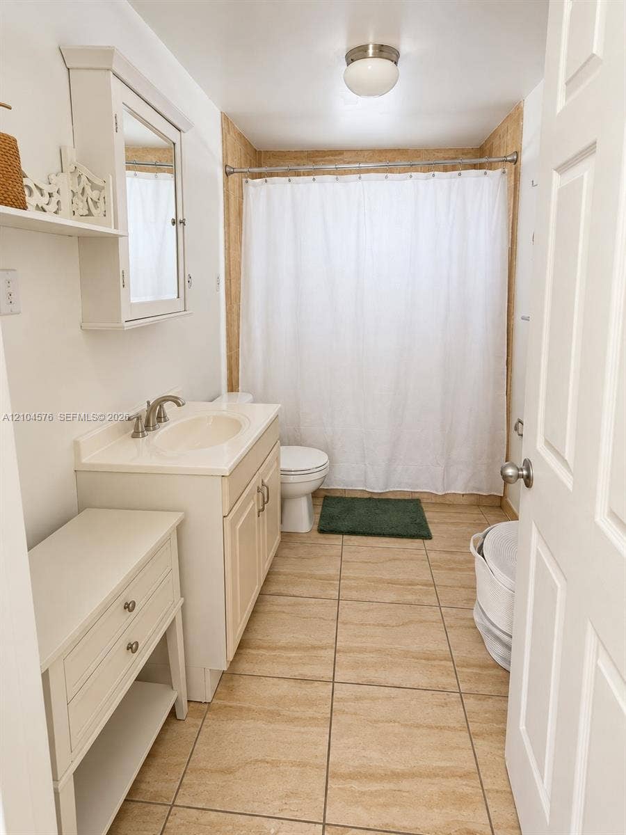 9755 SW 54th Street, Miami, Miami, FL 33165 Bathroom featuring large-format stone-finish floor tiling, a white vanity cabinet with an integrated sink, a wall-mounted mirrored medicine cabinet, and a shower-tub combination with full-height tile surround