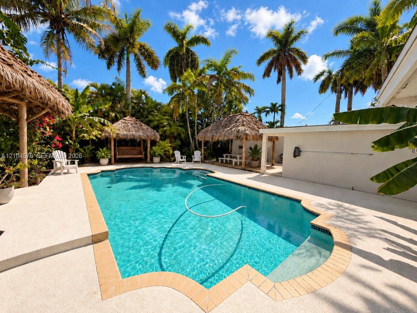 9755 SW 54th Street, Miami, Miami, FL 33165 In-ground swimming pool with a tan brick border, surrounded by concrete decking and multiple thatched-roof structures