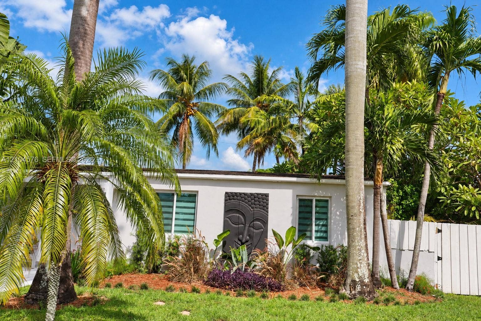 9755 SW 54th Street, Miami, Miami, FL 33165 Exterior featuring white stucco facade, manicured landscaping with mature palm trees, decorative wall relief, and perimeter fencing