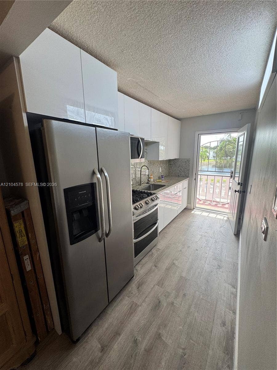 20320 NE 2nd Avenue, #22, Miami Gardens, Miami Gardens, FL 33179 Kitchen featuring gloss-finish cabinetry, stainless steel refrigerator and range, stone-surface countertops, and wood-finish flooring