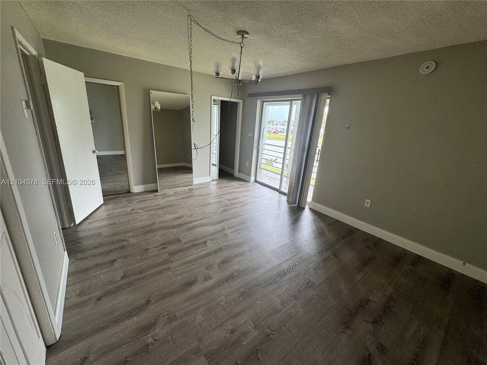 20320 NE 2nd Avenue, #22, Miami Gardens, Miami Gardens, FL 33179 Interior space featuring wood-finish flooring, a full-length wall mirror, a hanging light fixture, and a sliding glass door providing external access