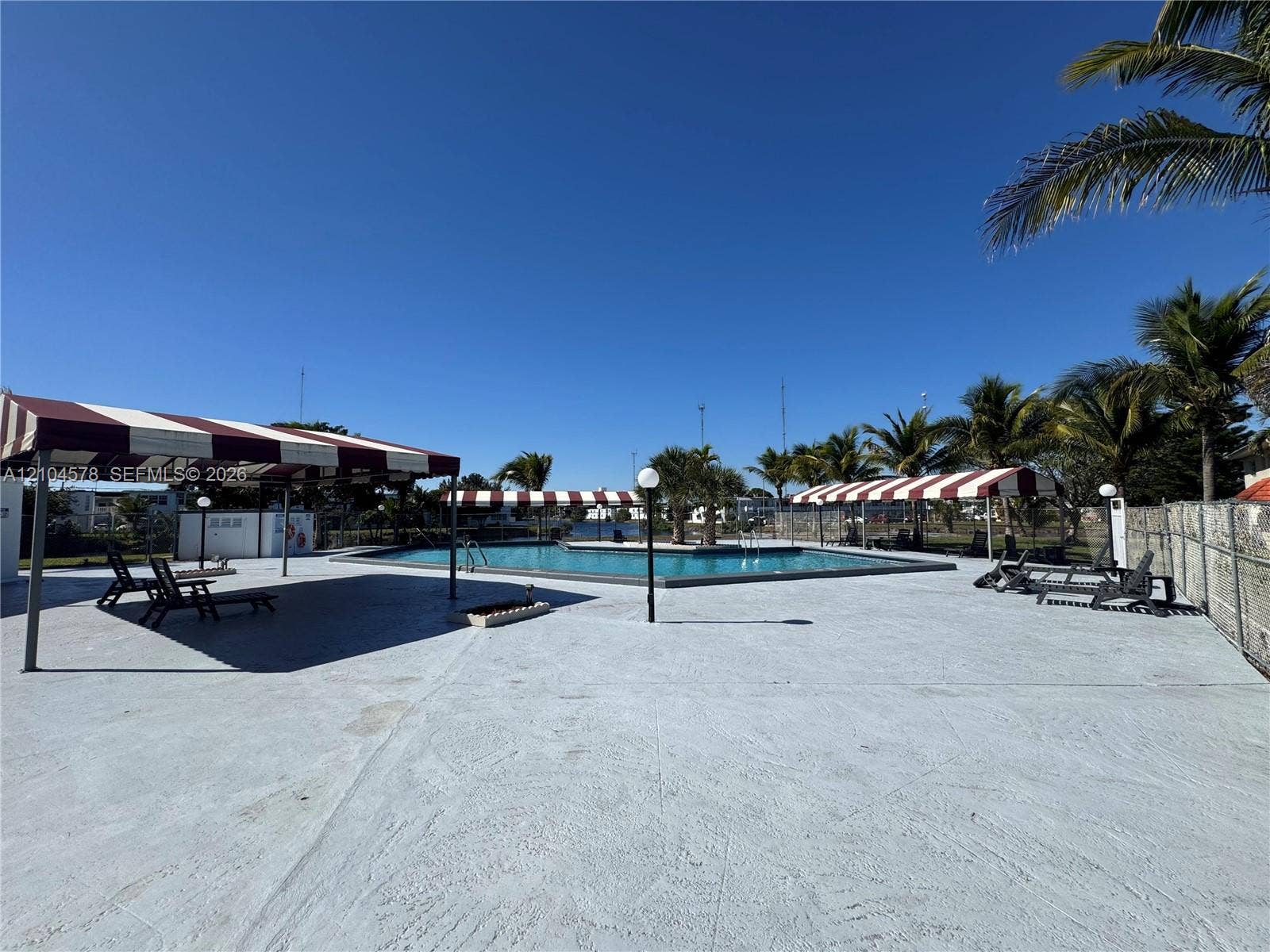 20320 NE 2nd Avenue, #22, Miami Gardens, Miami Gardens, FL 33179 Swimming pool area featuring expansive concrete decking, multi-sectioned fabric canopies, pole-mounted globe lighting, and mature palm trees