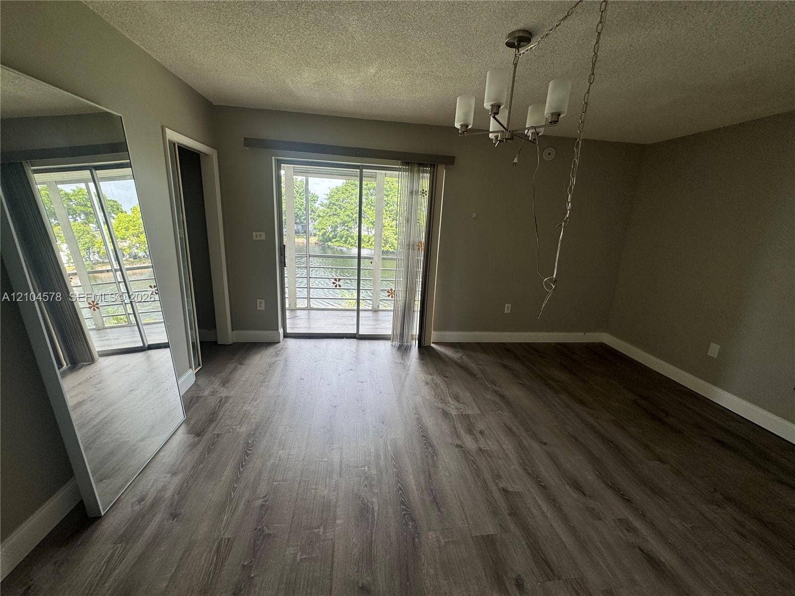 20320 NE 2nd Avenue, #22, Miami Gardens, Miami Gardens, FL 33179 Wood-finish flooring, full-length mirrored wall panels, multi-arm chandelier with glass shades, and sliding glass doors opening to a screened balcony
