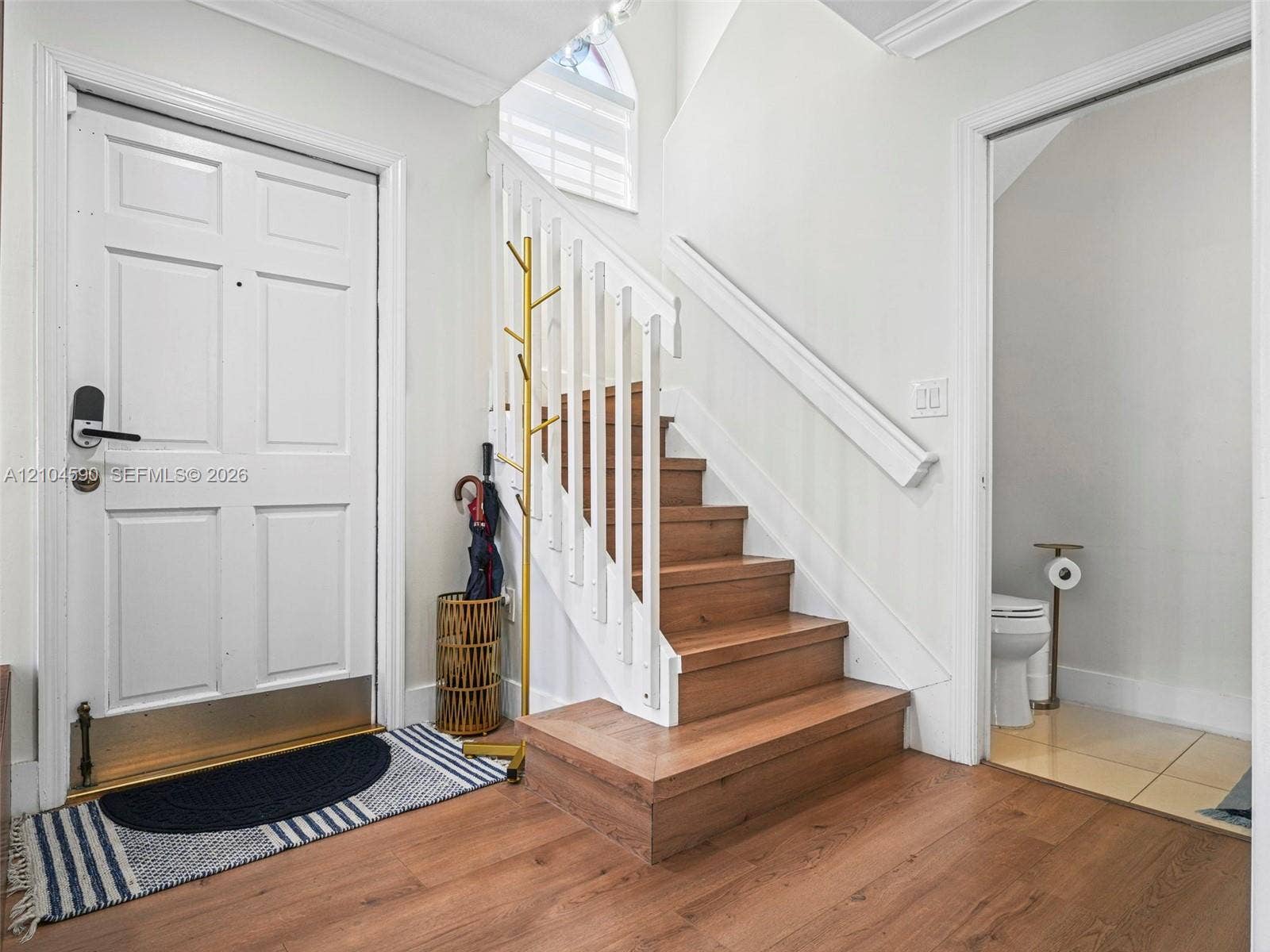 Foyer featuring wood-finish flooring, a staircase with wood-finish treads and white balusters, crown molding, and a vaulted arched window