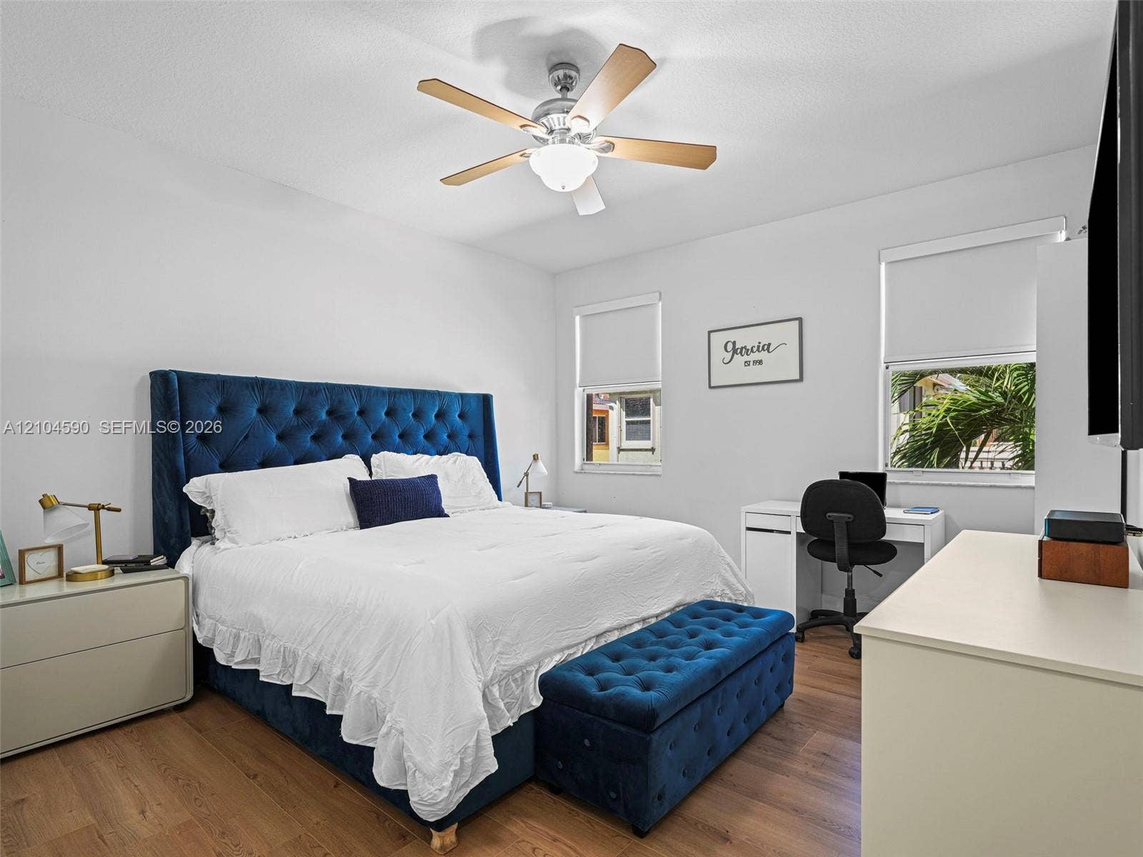 Wood-finish flooring, dual windows with roller shades, and a ceiling fan with integrated light fixture
