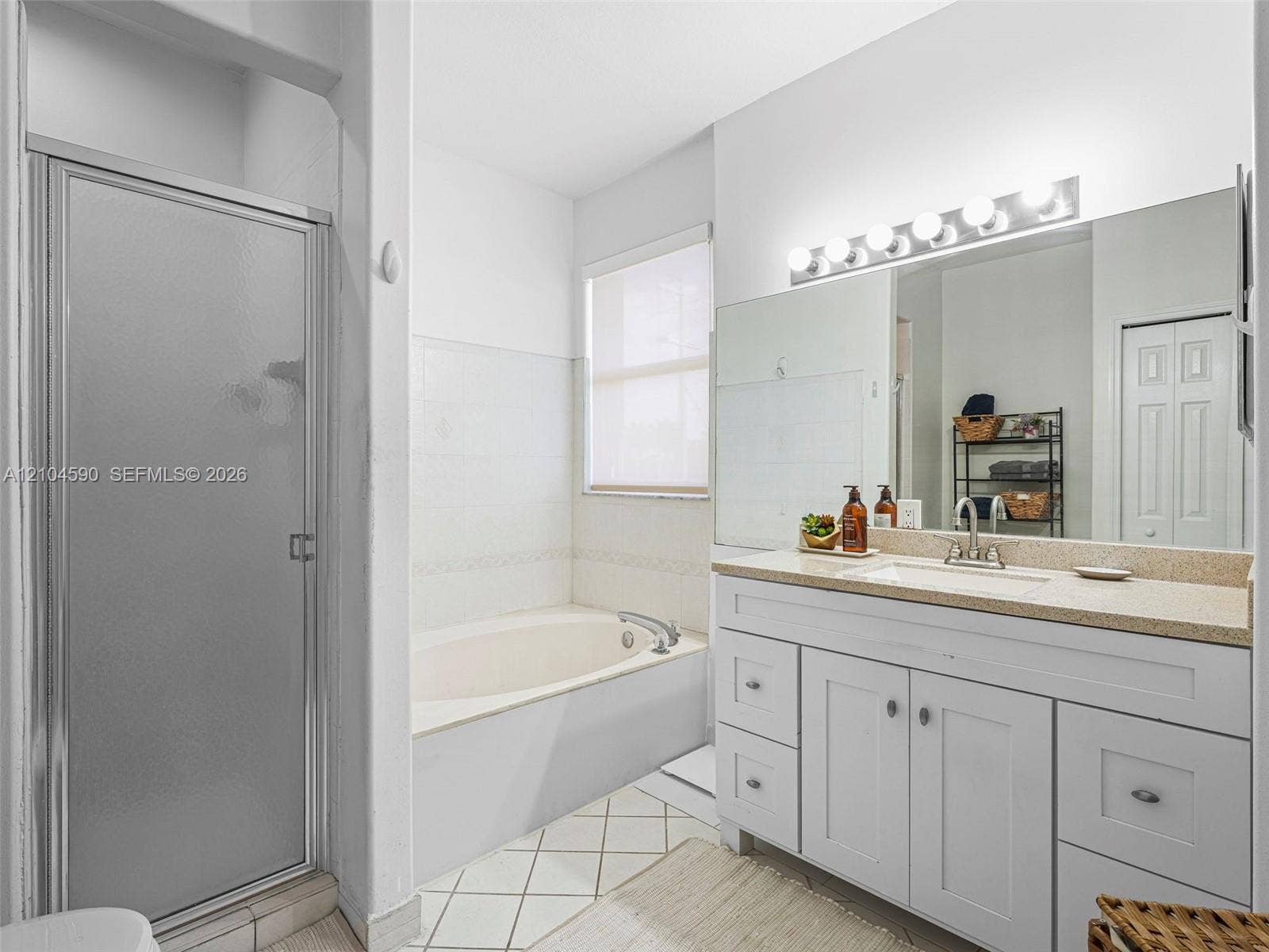 Bathroom featuring a white vanity with integrated basin, light-toned countertop, large wall-mounted mirror, separate soaking tub, and a glass-enclosed shower