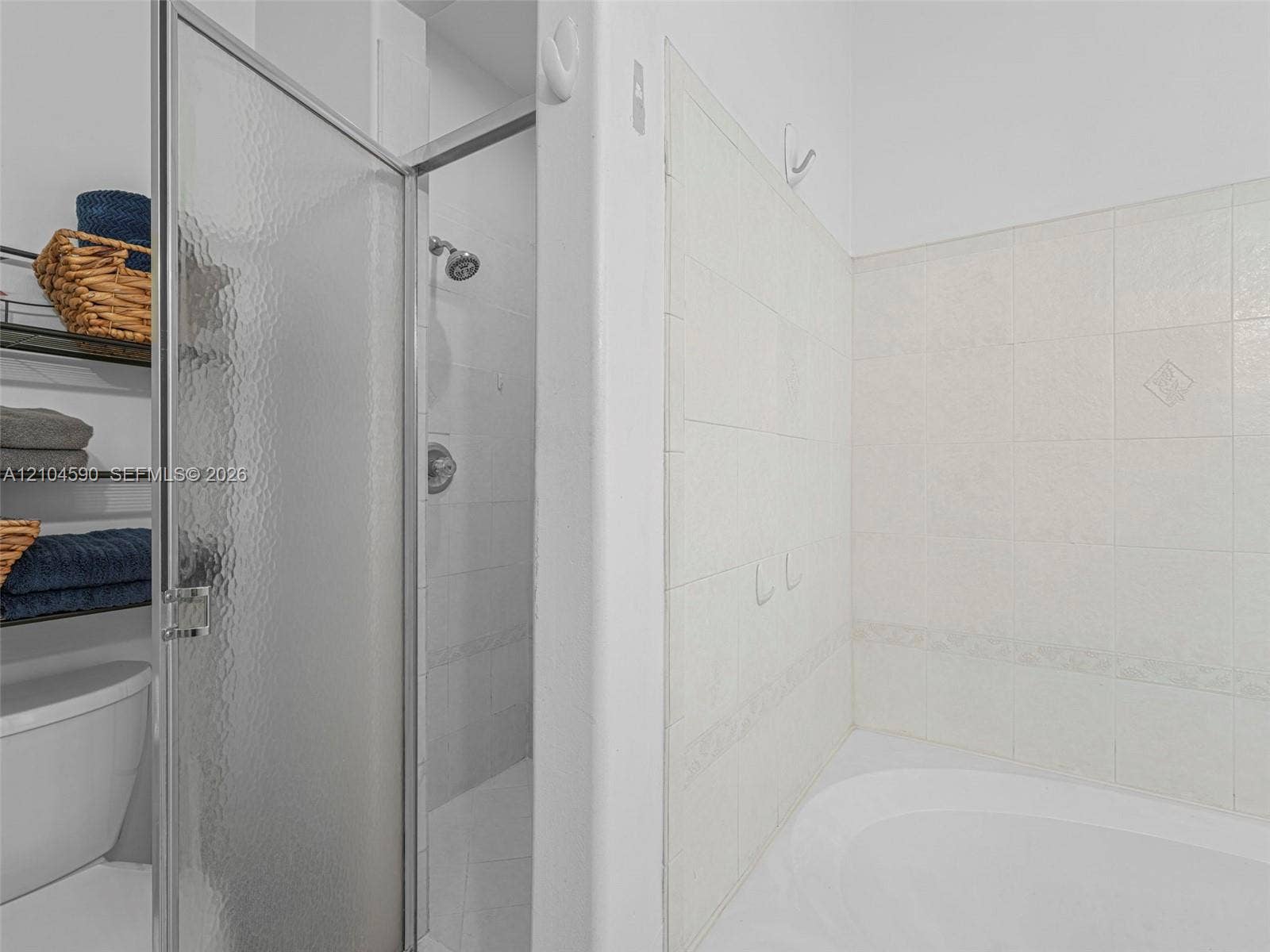 Shower stall with a textured glass door, chrome shower head, and large-format tile surround, accompanied by an integrated soaking tub featuring decorative tile detailing
