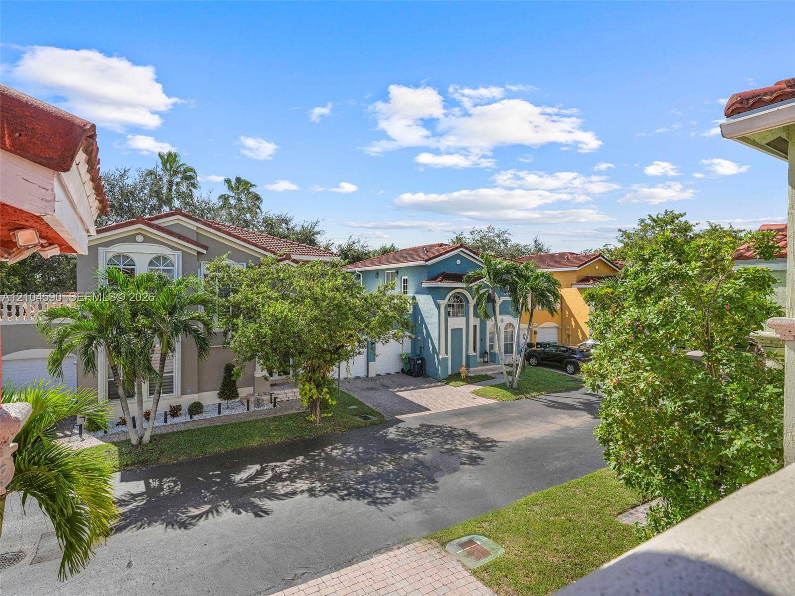 Multi-story residence featuring a tile roof, stucco exterior, paved driveway, and mature landscaping