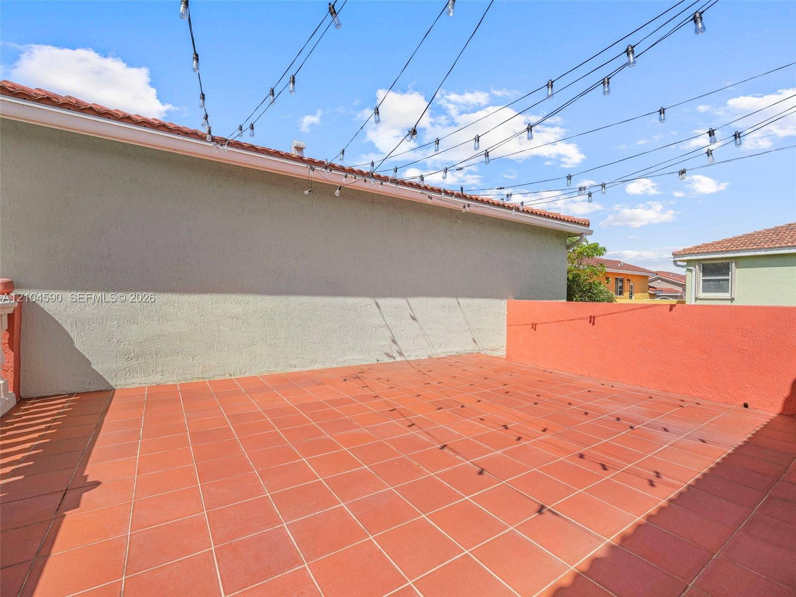 Outdoor terrace featuring terra cotta tile flooring, solid perimeter walls, and overhead string lighting