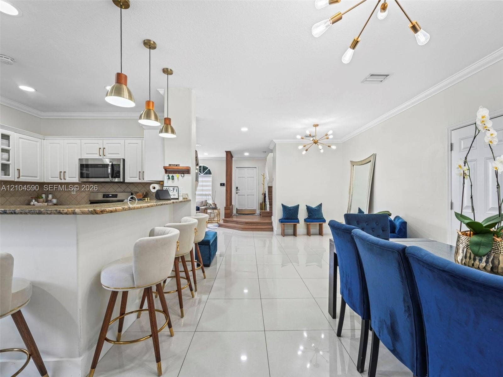 Open-concept interior featuring large-format tile flooring, stone-surfaced peninsula, white cabinetry, and multi-light brushed metallic chandeliers