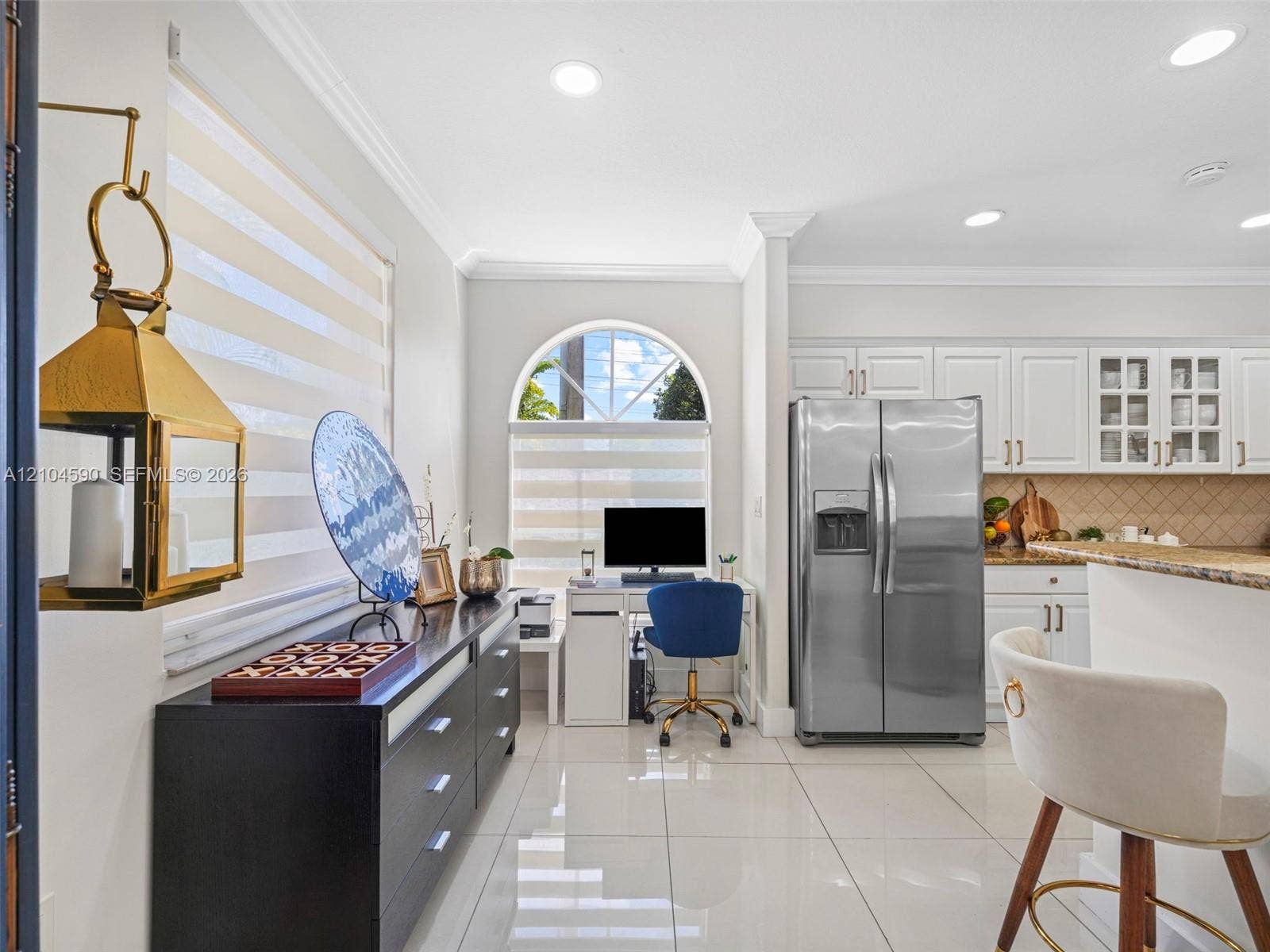Kitchen featuring white cabinetry with glass-front uppers, stainless steel refrigerator, stone countertops, arched window, and large-format porcelain tile flooring
