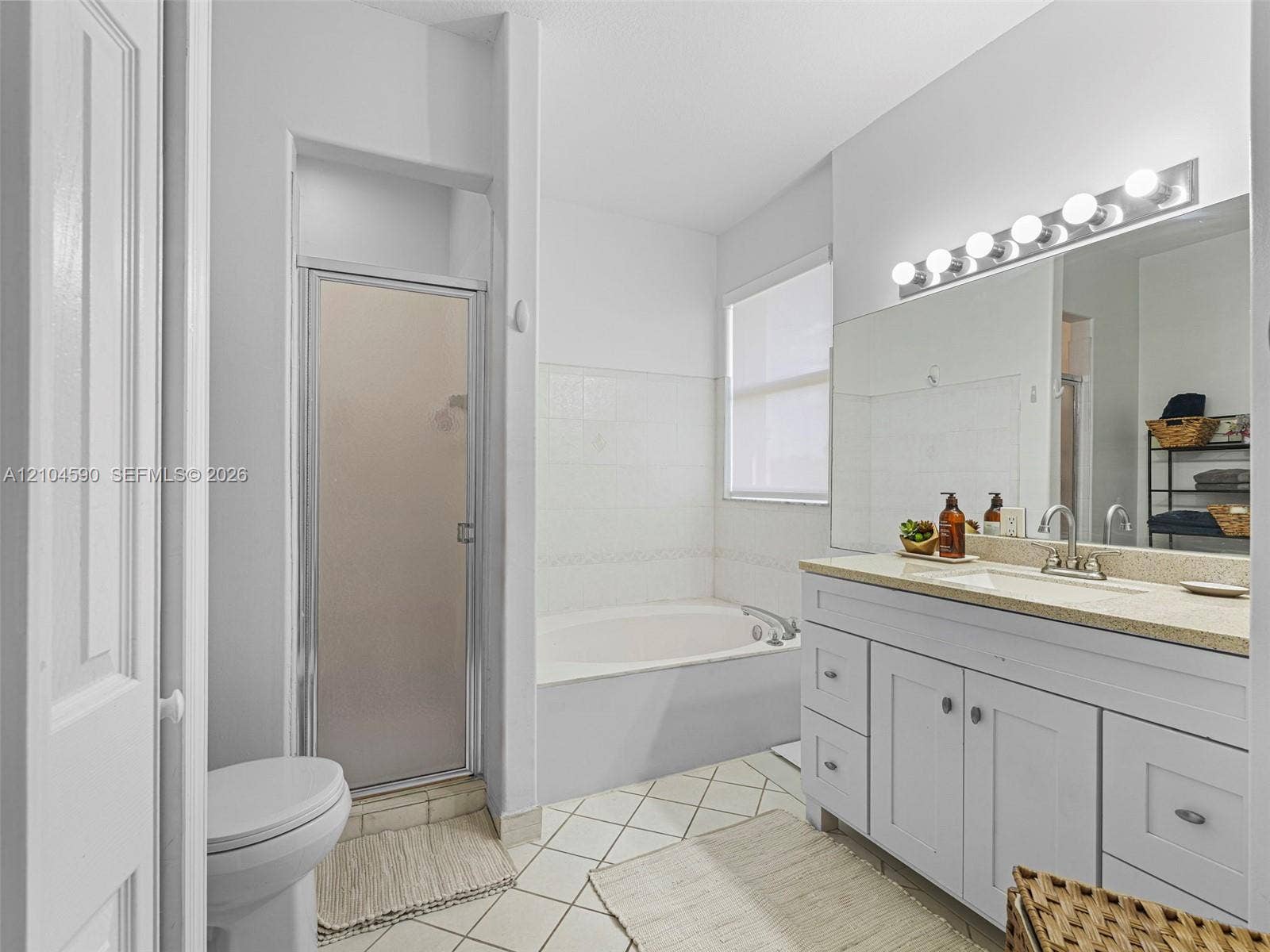 Bathroom featuring a vanity with integrated sink and stone-composite countertop, full-width wall mirror, separate shower stall with glass door, and soaking tub with tiled surround