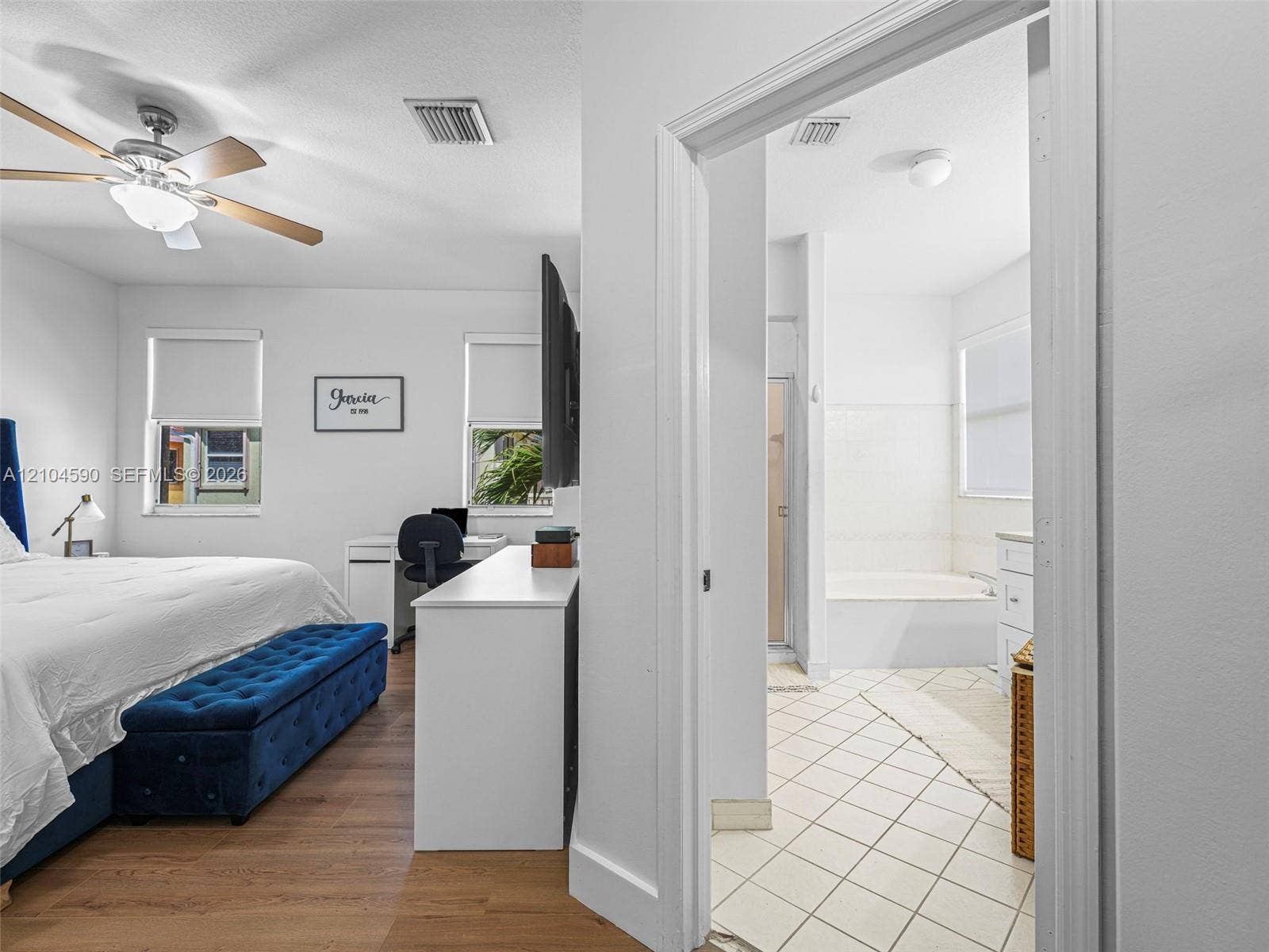 Bedroom featuring wood-finish flooring and a ceiling fan with integrated lighting, paired with a bathroom containing tile flooring and a tub-shower combination