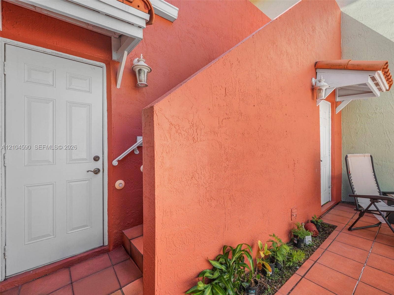 Stucco exterior featuring dual entry doors, terra cotta tile flooring, decorative wall-mounted light fixtures, and tiled roof overhangs