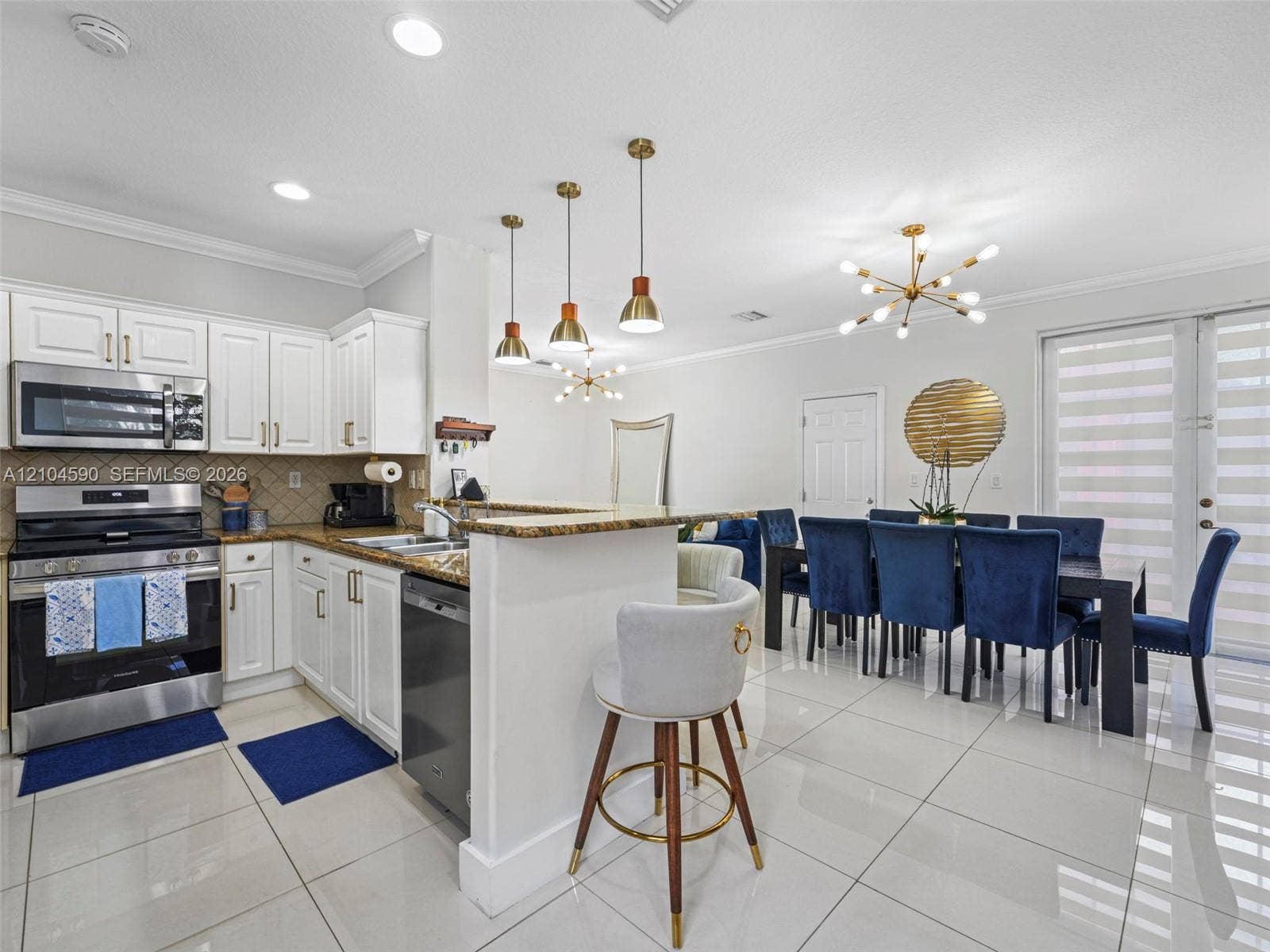 Kitchen featuring white cabinetry, stone countertops, stainless steel appliances, tiered pendant lighting, and polished floor tile