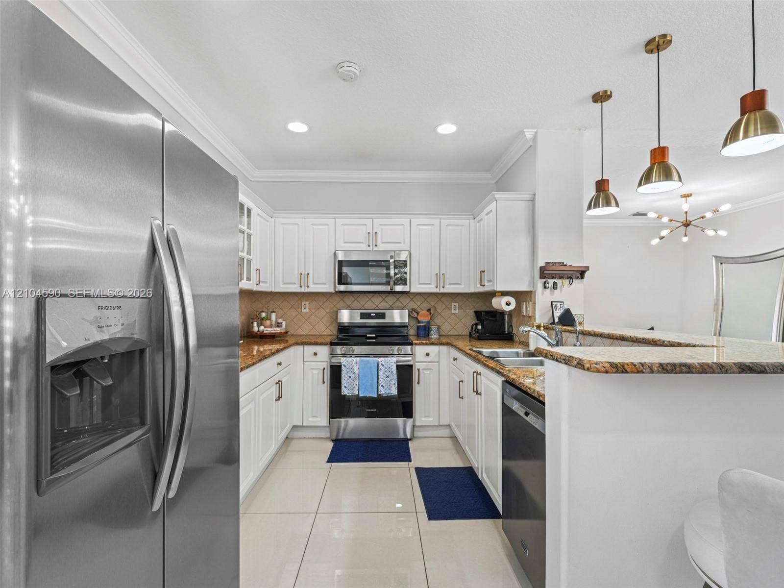 Kitchen featuring white shaker-style cabinetry, stone-finish countertops, stainless steel appliances, tile flooring, and pendant lighting