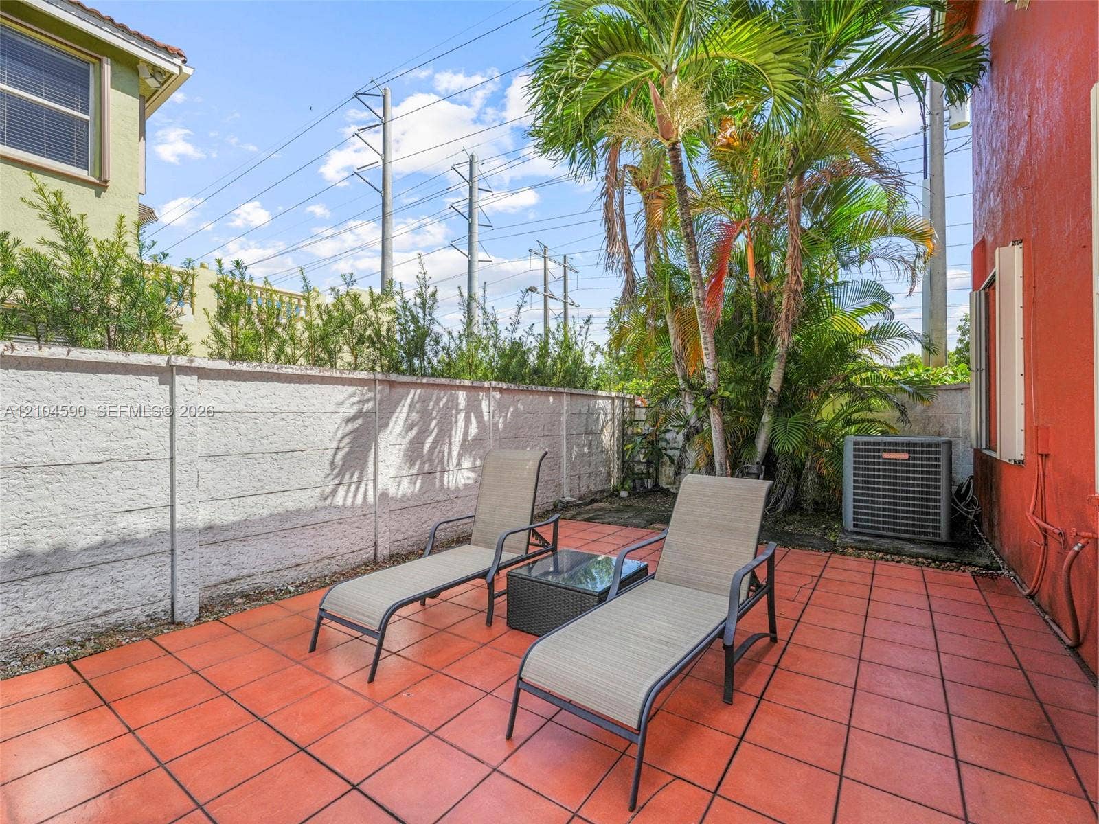 Private patio featuring red tile flooring, a perimeter concrete wall, and mature palm trees