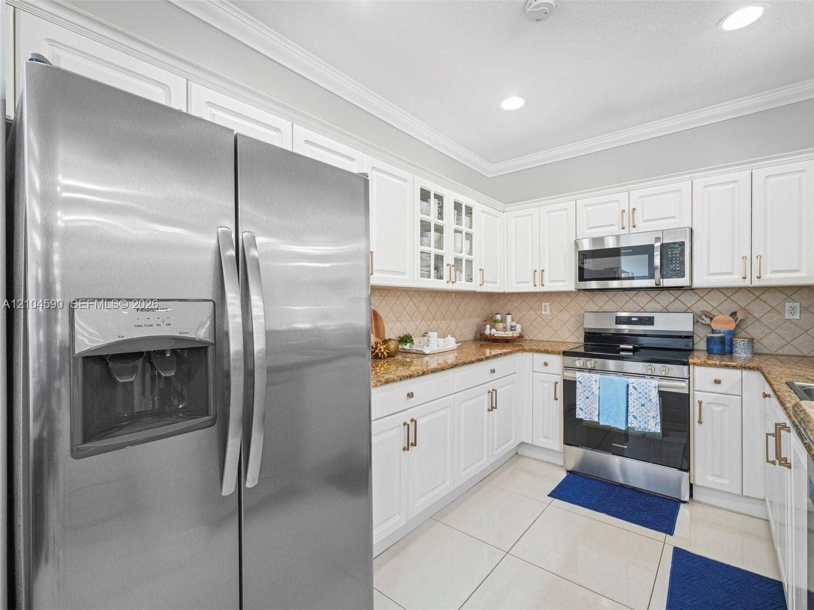 Kitchen featuring white cabinetry, stone countertops, stainless steel appliances, glass-front upper cabinet doors, and tile flooring