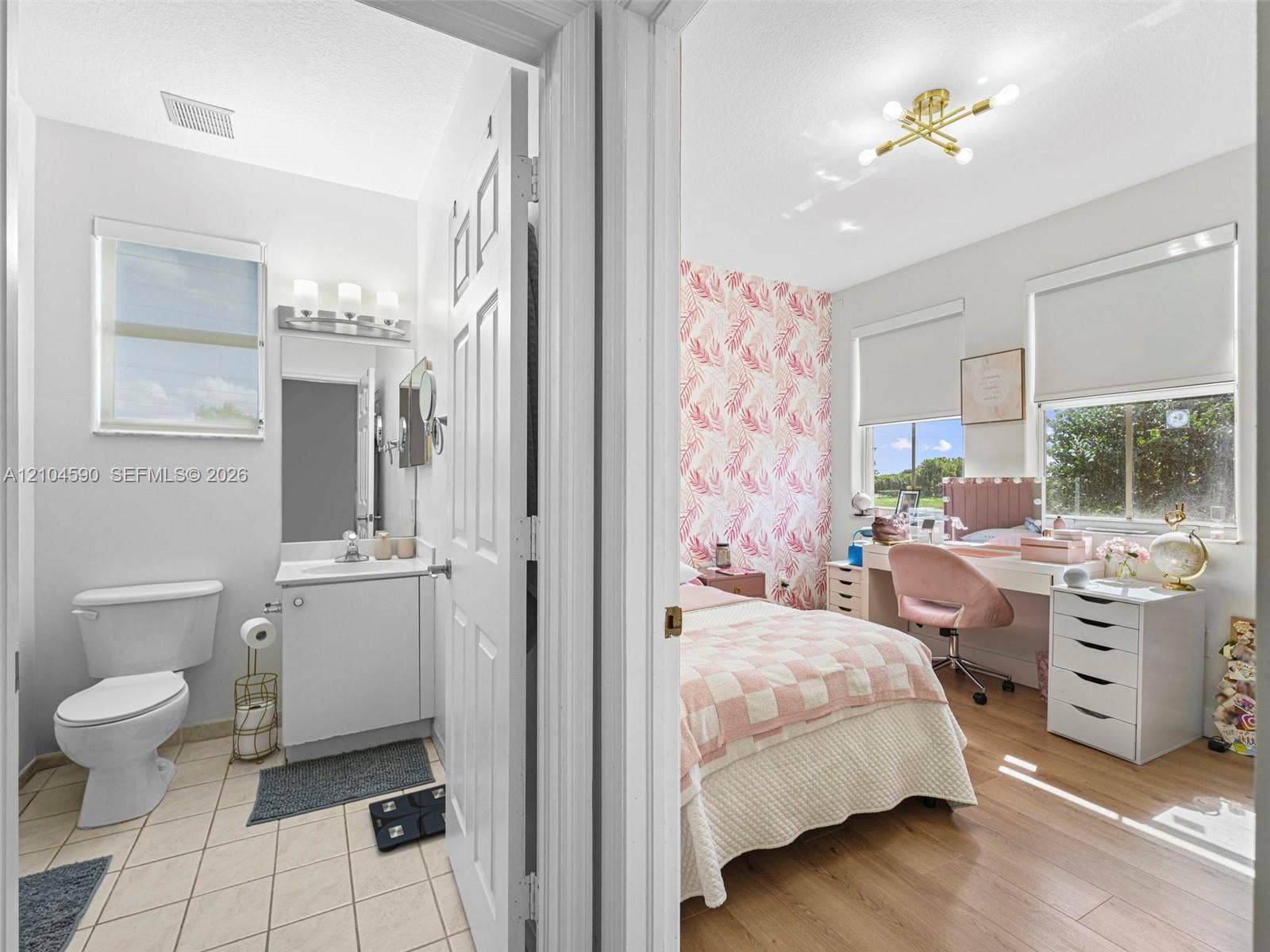 Bathroom featuring a white vanity with an integrated sink, three-light fixture, and ceramic tile flooring, paired with a bedroom showcasing wood-finish flooring, a multi-arm modern light fixture, and large windows
