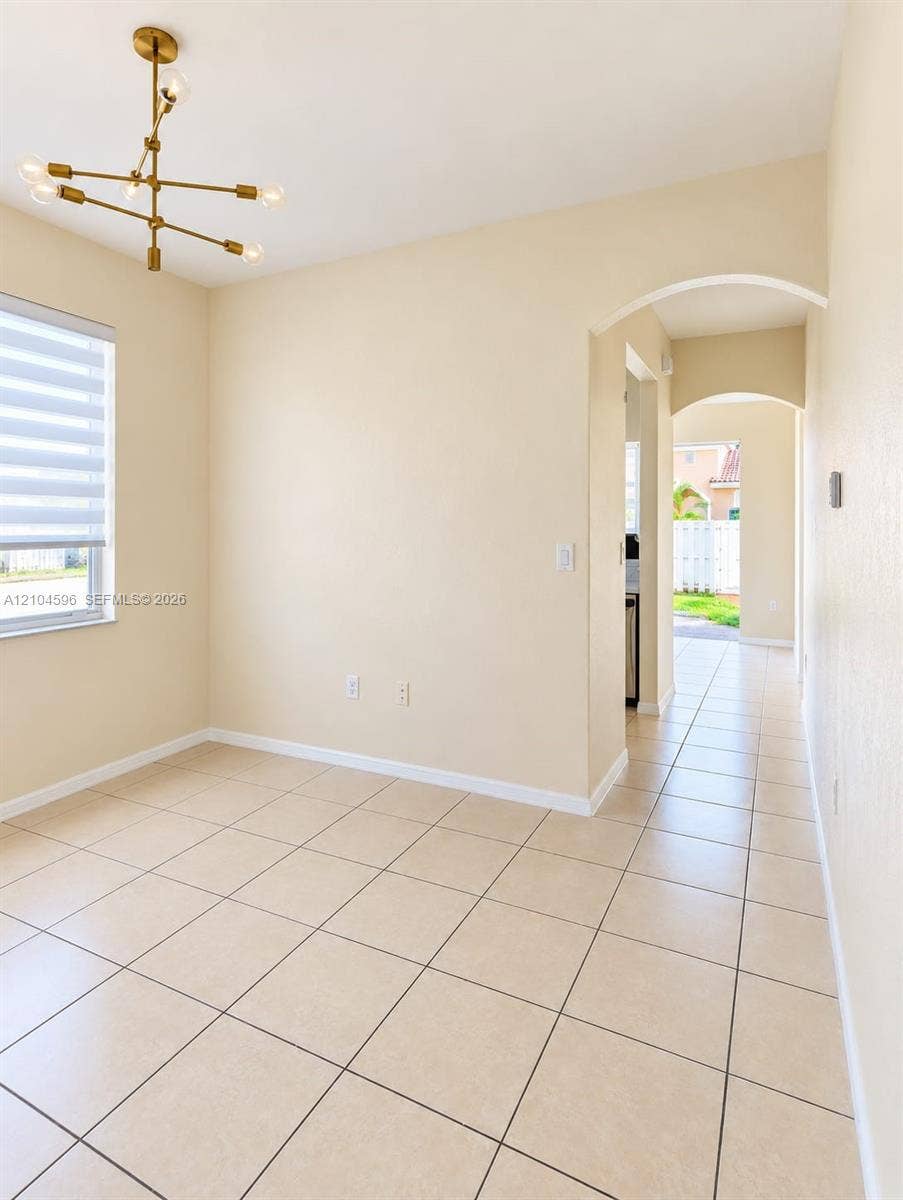 10968 SW 236th Terrace, Homestead, Homestead, FL 33032 Interior space featuring large-format tile flooring, a modern multi-arm brass finish chandelier, neutral wall tones, and architectural arched doorways