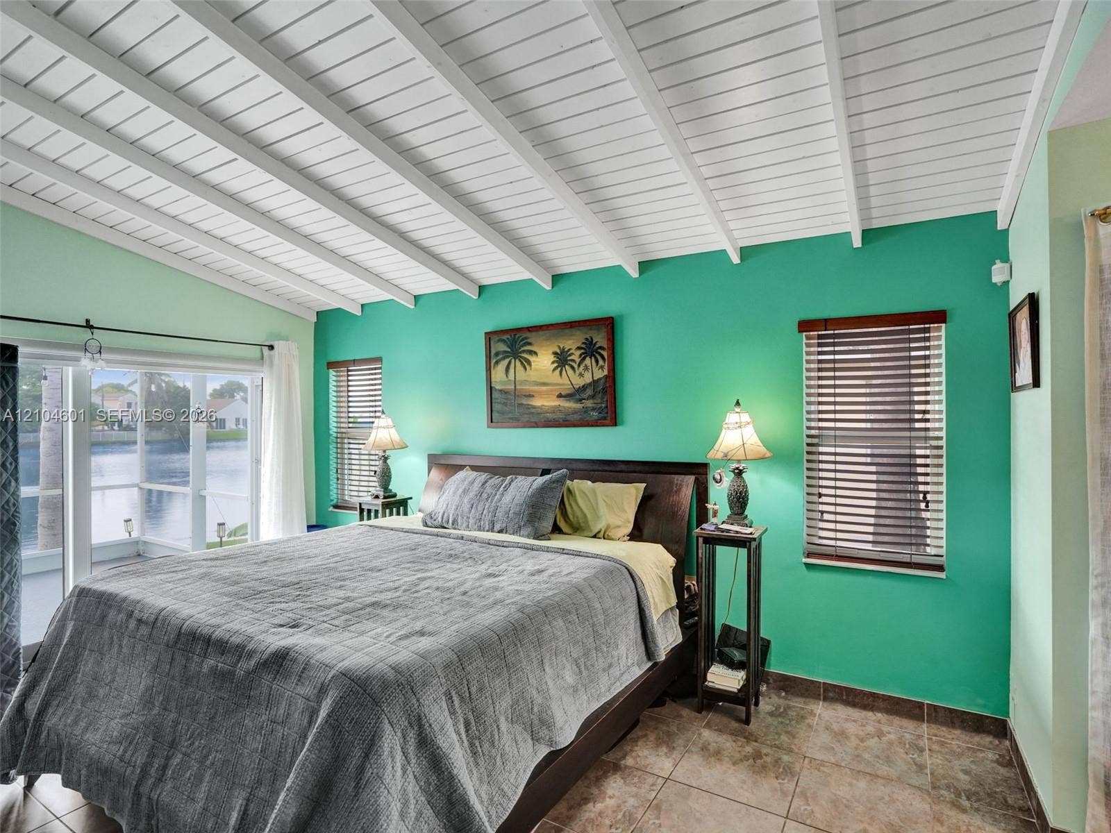 Vaulted ceiling with exposed white beams, tile flooring, and multiple windows with horizontal blinds