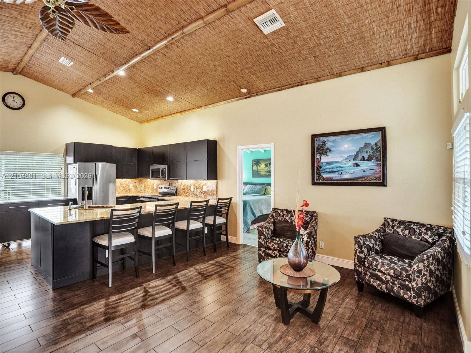 Vaulted ceiling with textured woven-fiber detailing, dark wood-finish cabinetry, stone-surface kitchen island, and wood-finish flooring