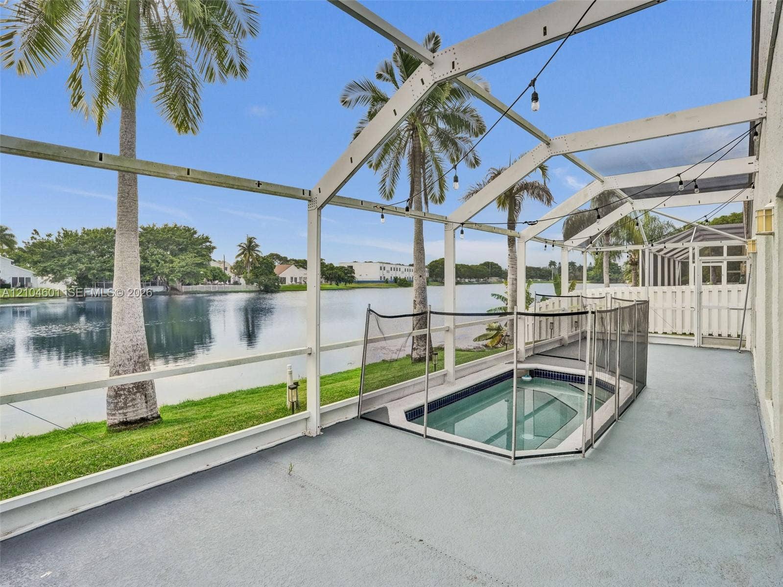 Screened-in patio featuring a built-in spa, concrete flooring, and water frontage