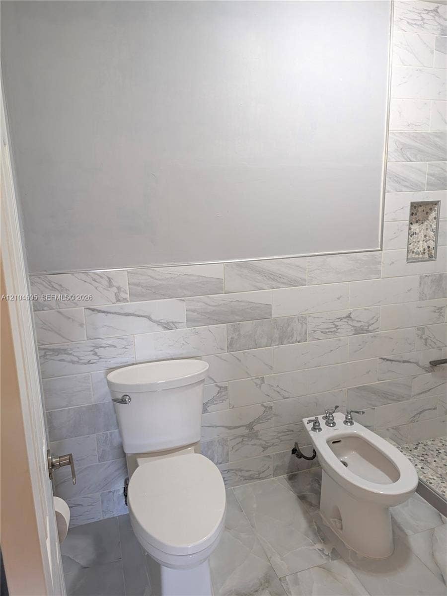 Wall-mounted mirror, large-format tile flooring, horizontal stone-pattern wall tiling, integrated wall niche, and porcelain plumbing fixtures