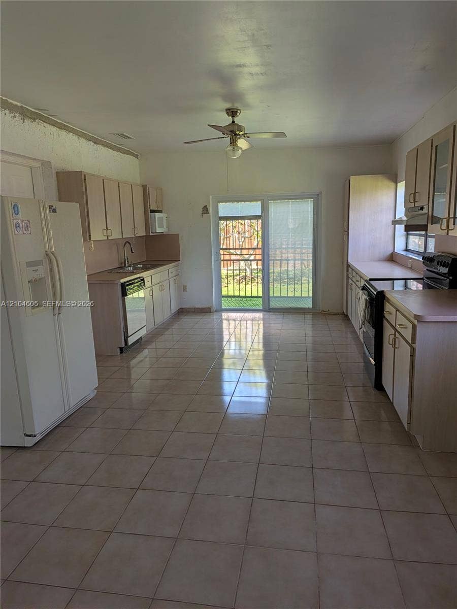 Kitchen featuring light-finish cabinetry, ceramic tile flooring, a dual-basin stainless steel sink, a ceiling fan, and sliding glass doors
