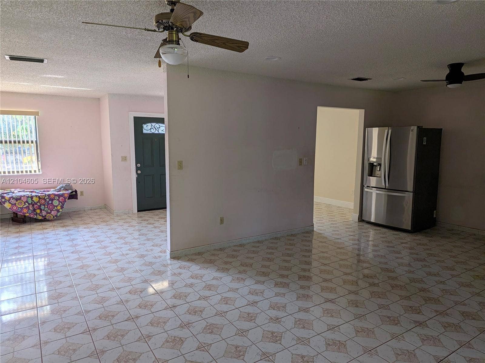 Tiled flooring featuring a geometric pattern, stainless steel refrigerator, two ceiling fans, and an exterior door with a decorative glass insert