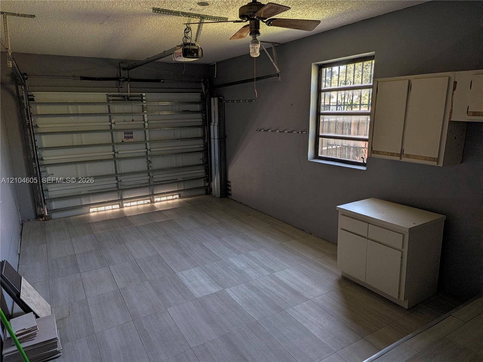 Garage featuring tile flooring, metal sectional garage door, built-in wall and base cabinetry, and ceiling-mounted paddle fan