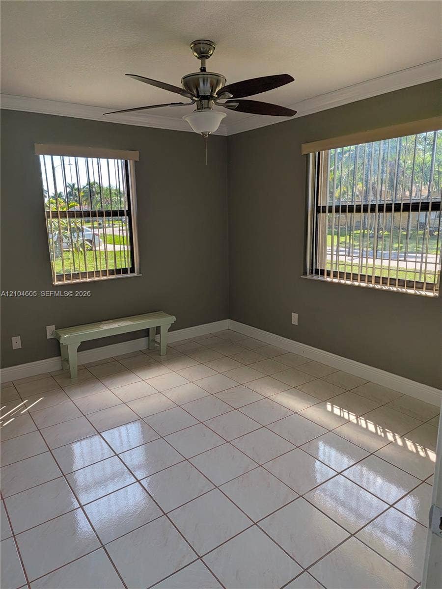 Interior room featuring neutral-toned walls, polished ceramic tile flooring, a multi-blade ceiling fan, and windows equipped with metal security bars