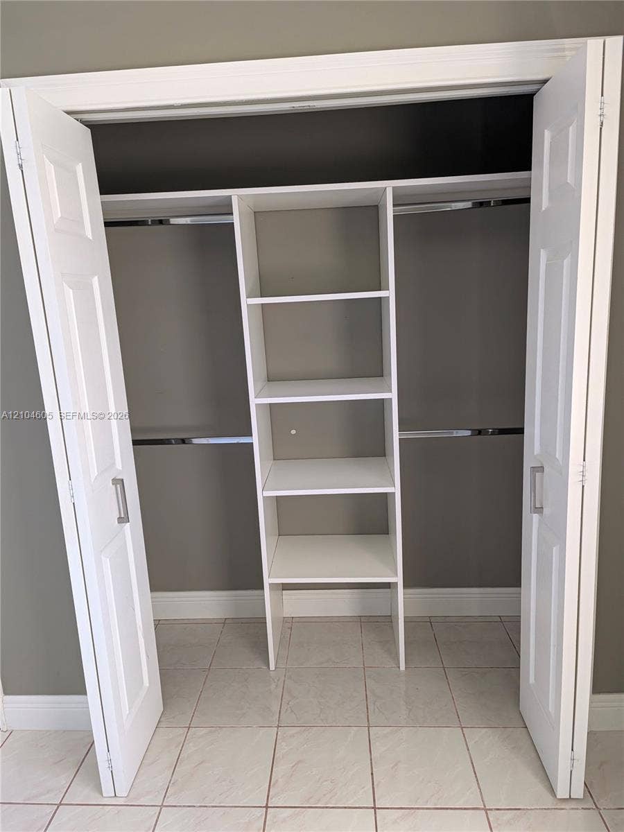 Reach-in closet featuring white bi-fold doors, chrome hanging rods, and integrated floor-to-ceiling shelving