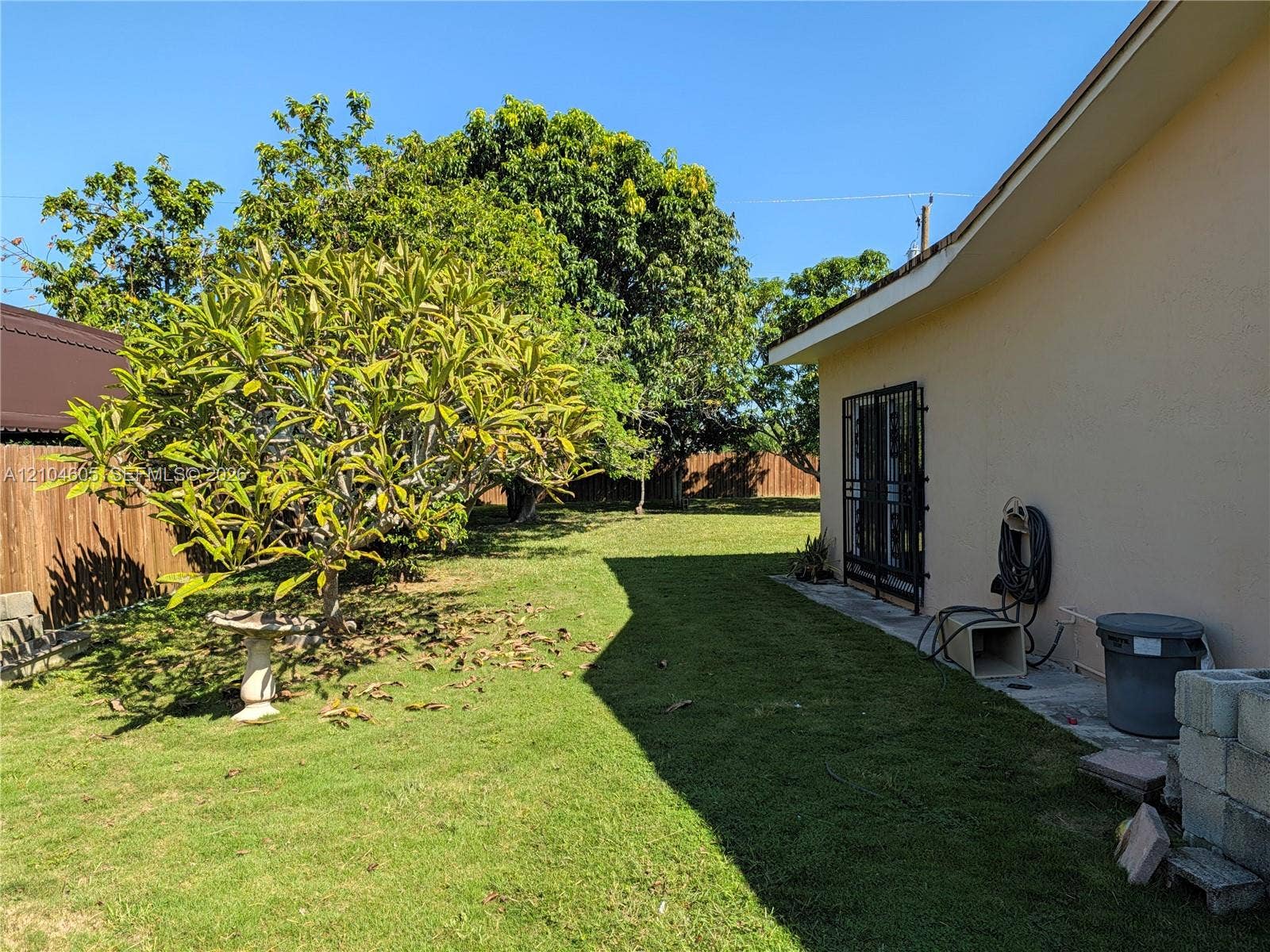 Expansive backyard featuring a grass lawn, mature trees, wood privacy fencing, and a concrete side patio