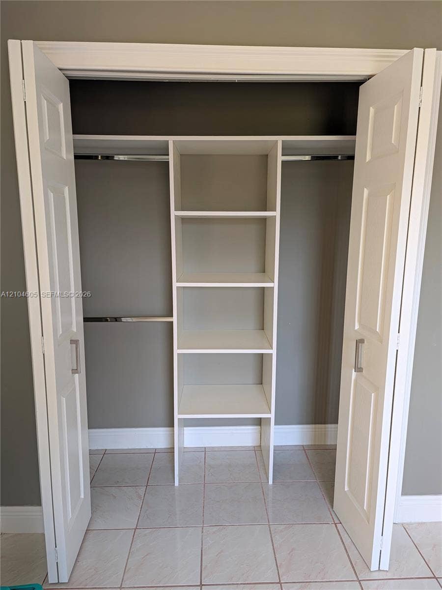 Closet featuring white bi-fold doors, built-in shelving, metal hanging rods, and light-toned tile flooring