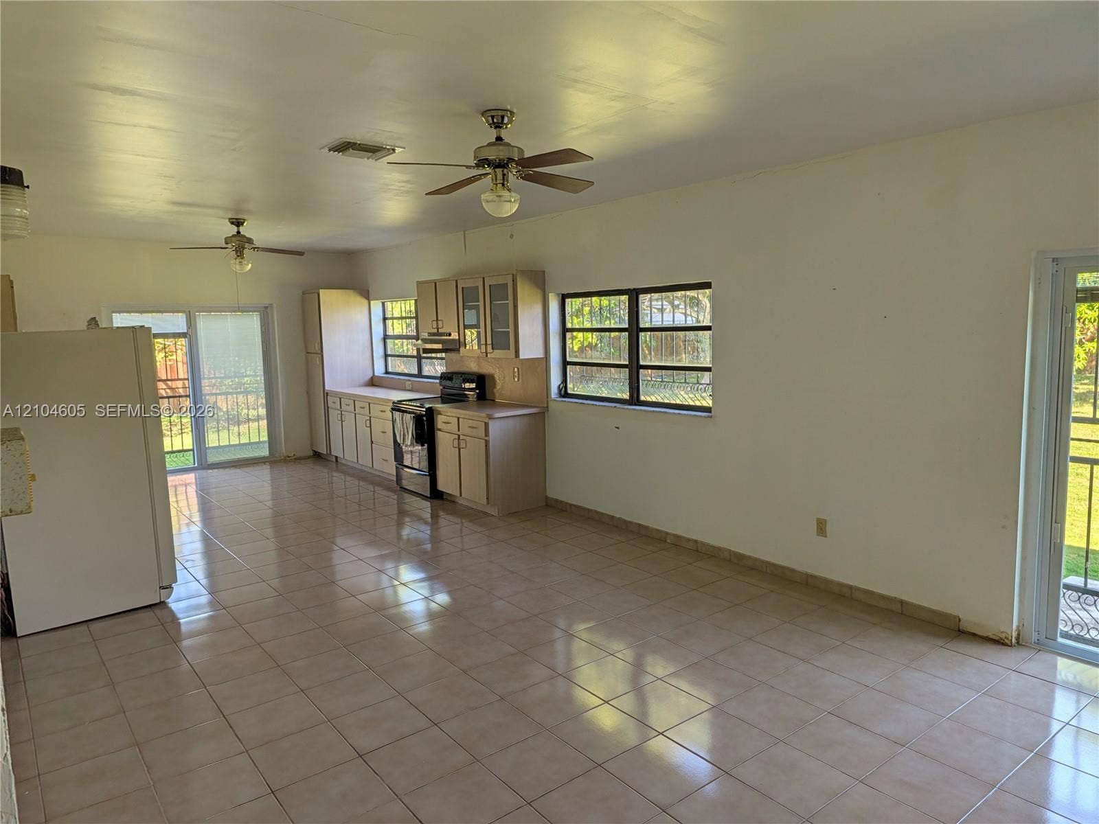 Open-concept kitchen featuring ceramic tile flooring, neutral cabinetry, dual ceiling fans, and two sliding glass exterior doors