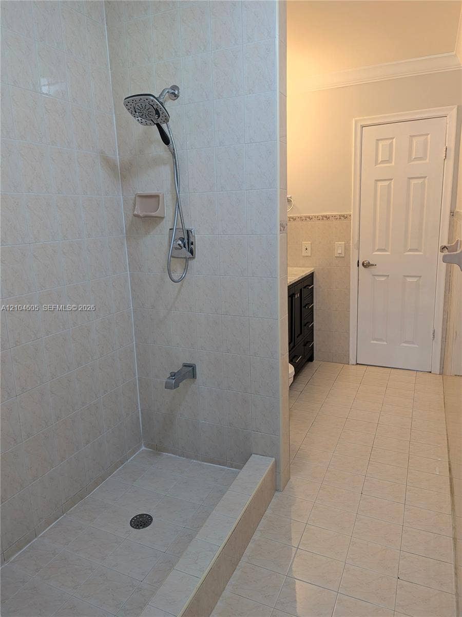Walk-in shower with floor-to-ceiling tile, adjustable handheld shower head, and built-in soap niche, paired with dark-finish cabinetry and neutral ceramic tile flooring
