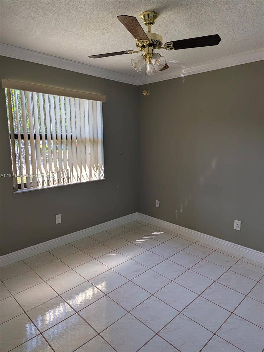 Neutral-toned interior space featuring light-colored tile flooring, crown molding, vertical window blinds, and a ceiling-mounted fan with integrated lighting